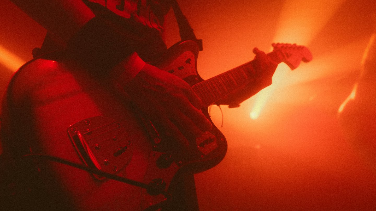 Handen van een muzikant die een elektrische gitaar bespelen op het podium.