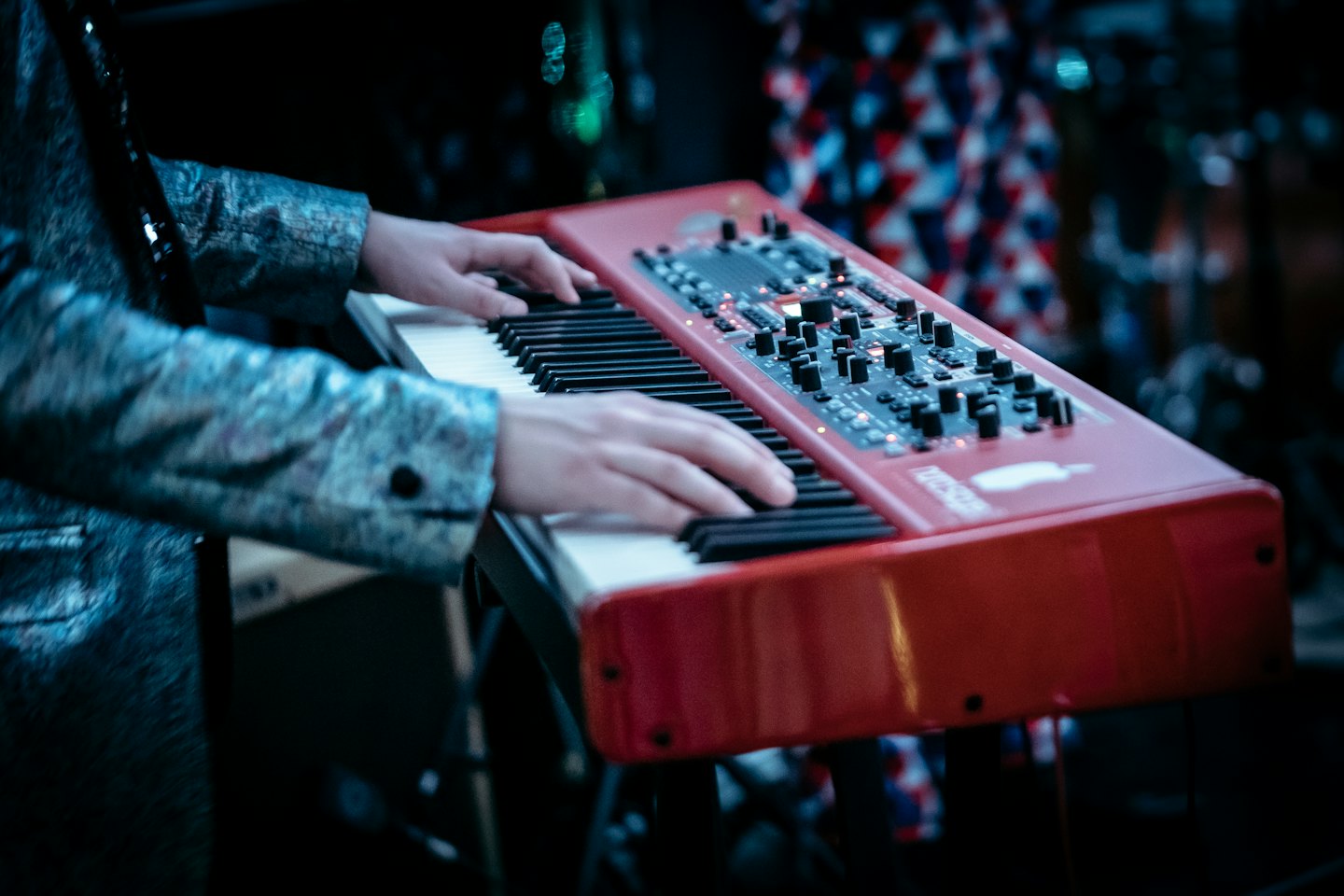 Een muzikant speelt op een rode keyboard synthesizer, gekleed in een blauwe jas.