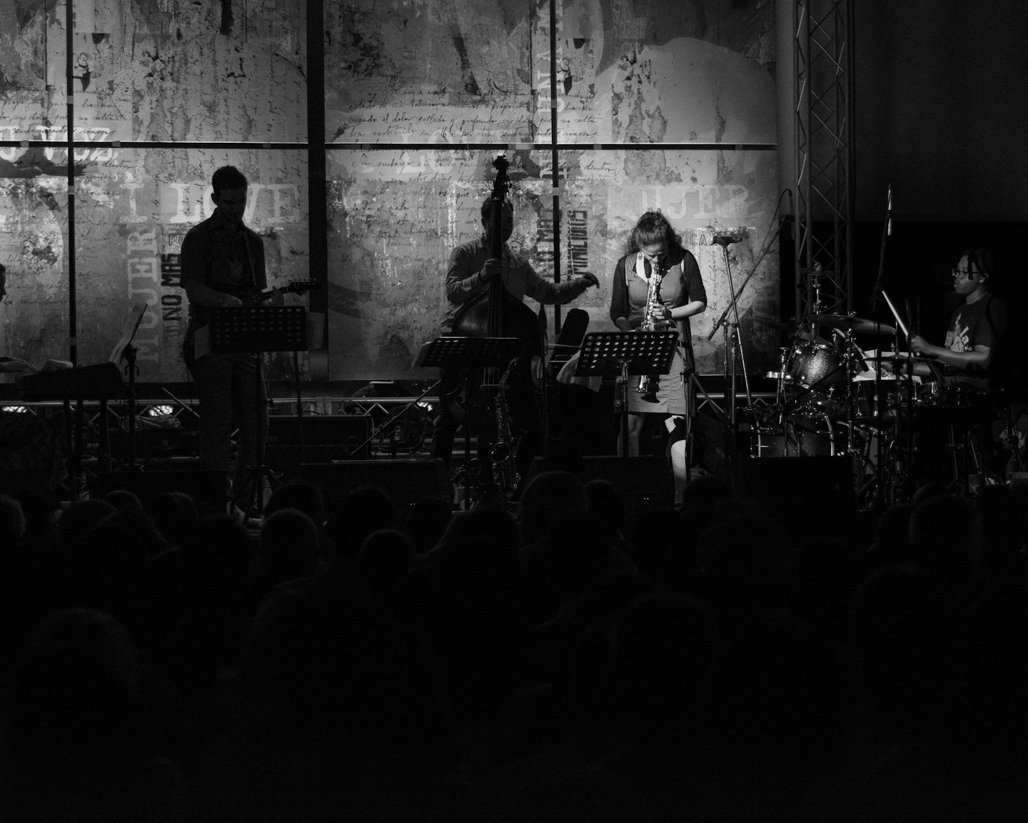Een band van vier personen treedt op op een podium met silhouetten van het publiek.