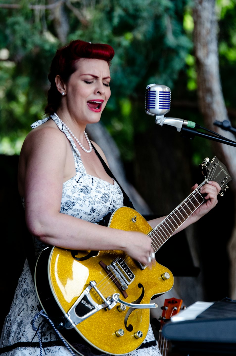 Vrouw met rood haar zingt in een vintage microfoon en speelt op een gouden gitaar.