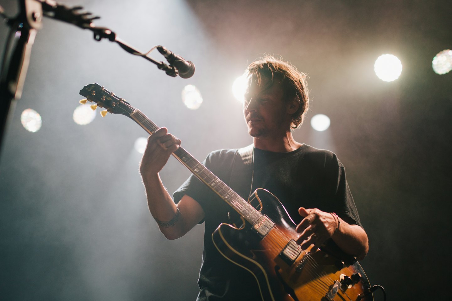 Man die elektrische gitaar speelt op een rokerig podium.